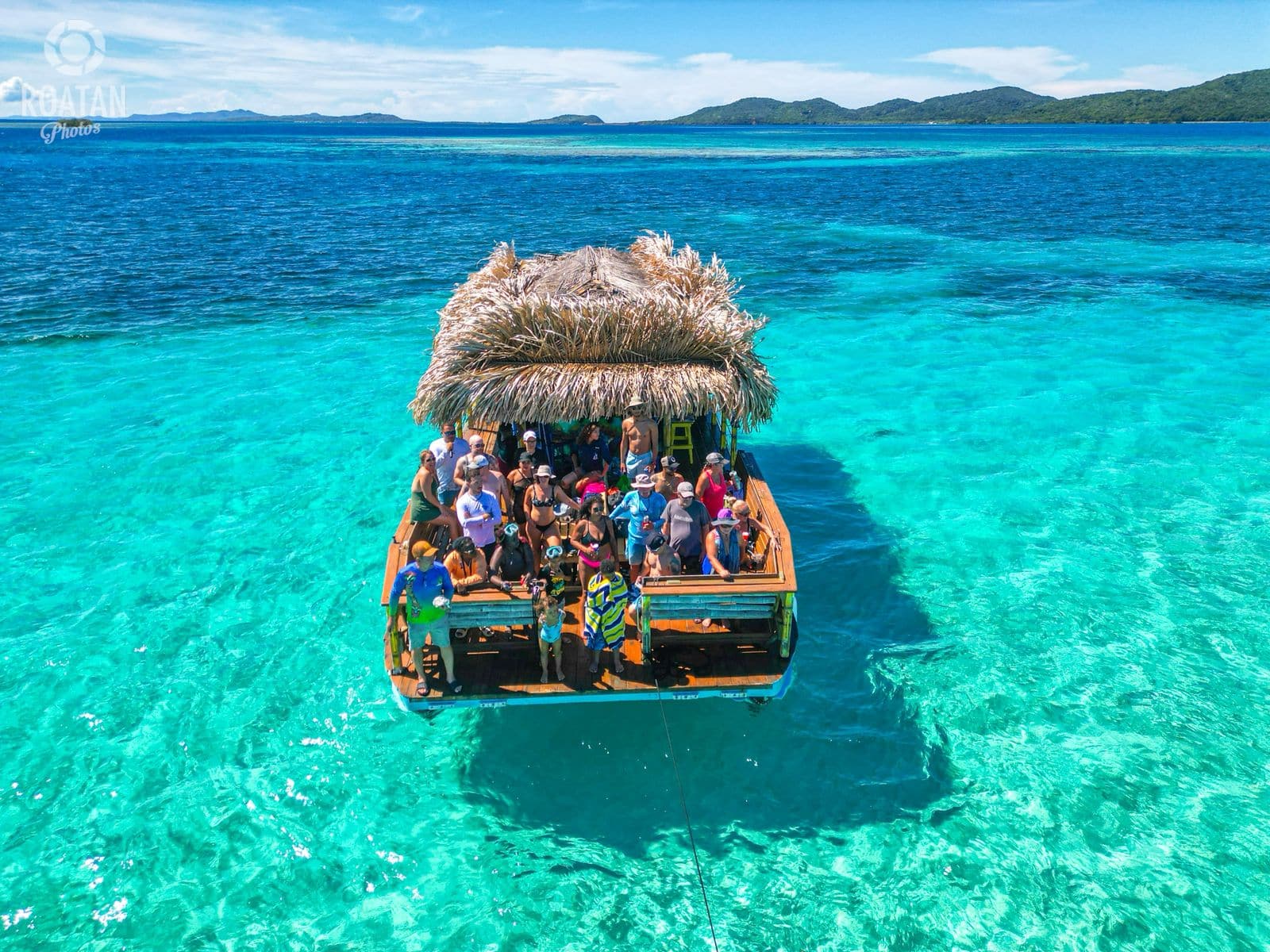 A vibrant Tiki boat filled with happy tourists enjoying a boat cruise in clear Caribbean waters near Roatan.