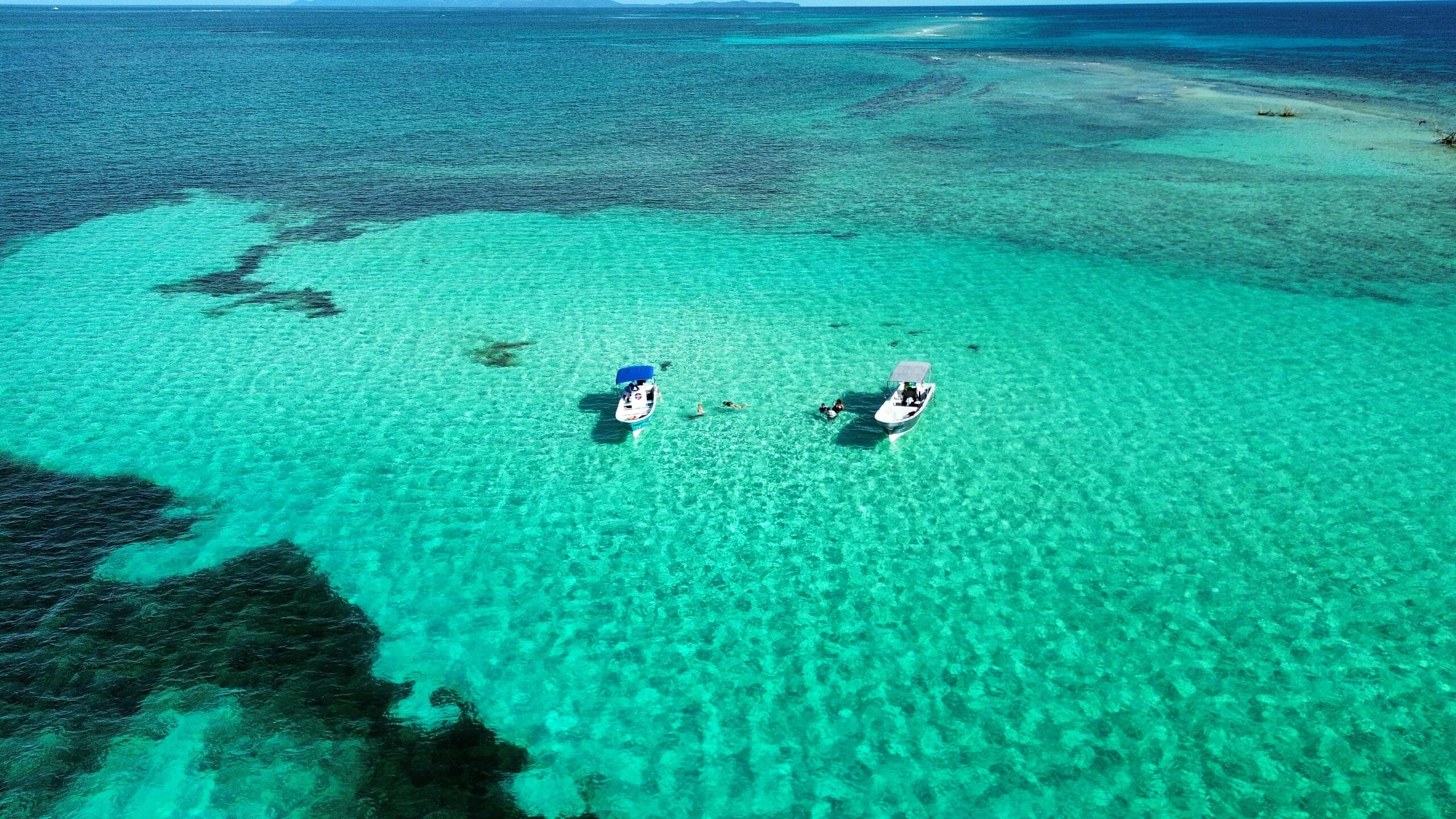 Vibrant turquoise waters with boats and swimmers off Roatan's coast. Enjoy water adventures in stunning Caribbean surroundings.